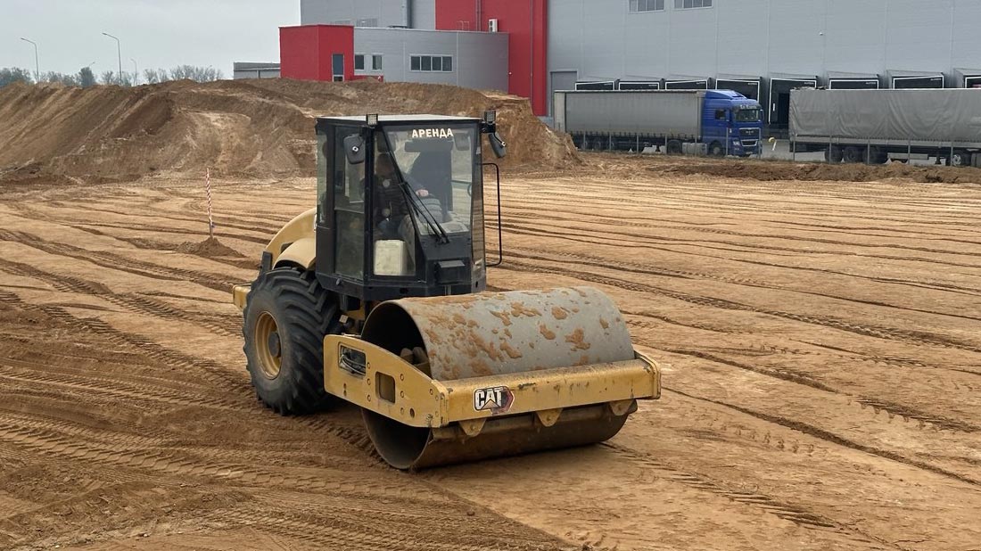 Аренда виброкатка грунтового Caterpillar для уплотнения песка под строительство складских помещений в Хатежино